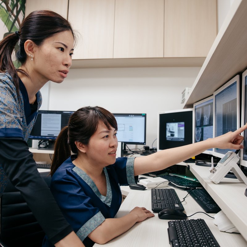 Two AARO radiation therapists at the planning console, reviewing a treatment plan together on a multi-monitor workstation.
