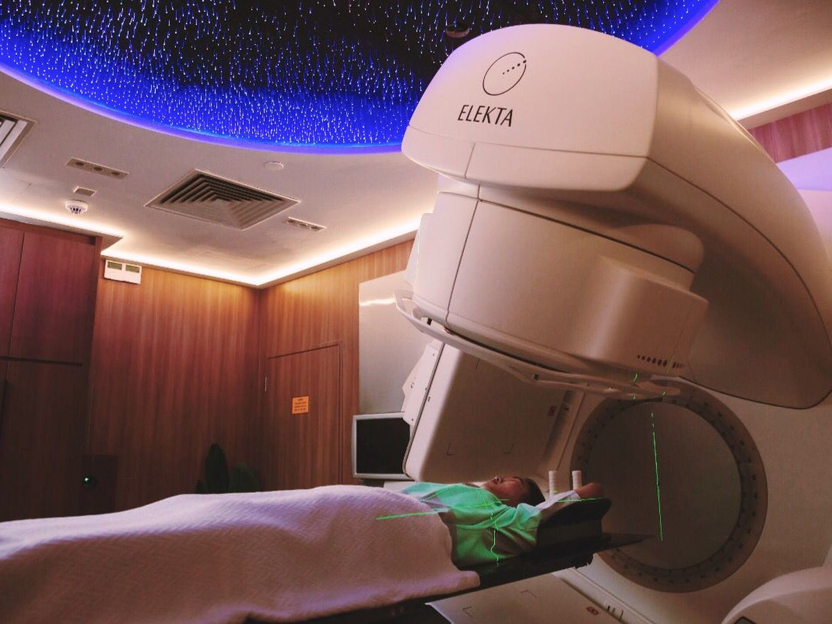 A patient comfortably positioned beneath the Elekta linear accelerator with green laser positioning lights and the signature starry ceiling above.